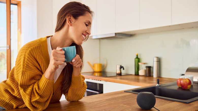 A woman in a kitchen looking at a smart speaker.