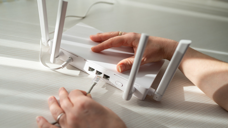 A person is inserting an Ethernet cable into a wireless router