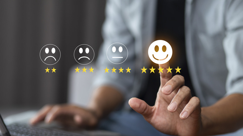 Person on a laptop with a hand pointing at smiley emojis ratings