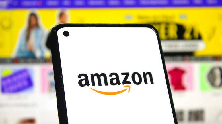 Amazon logo on smartphone screen with Amazon's website in the background
