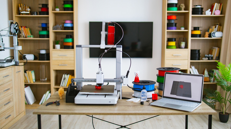 Desktop 3D printer surrounded by colorful filament spools and laptop workspace