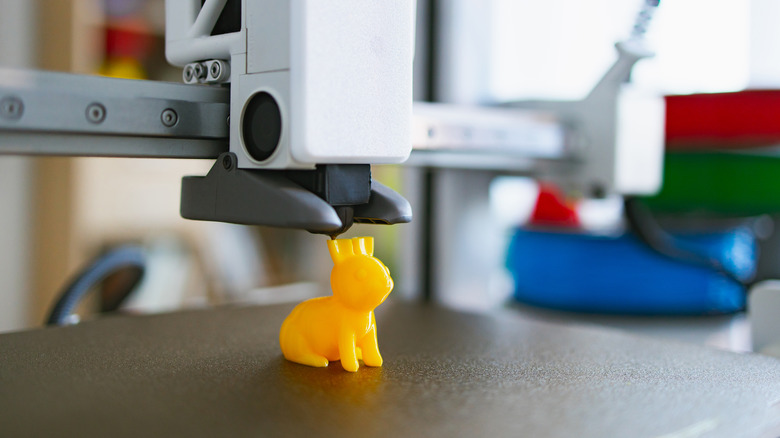 3D printer creating yellow model on textured build plate surface