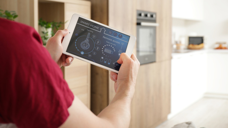 A person holding up a smart home tablet with smart device remote controls visible on the screen.