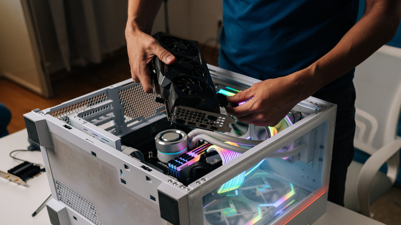 Person installing a graphics card into a desktop PC with RGB components on a desk
