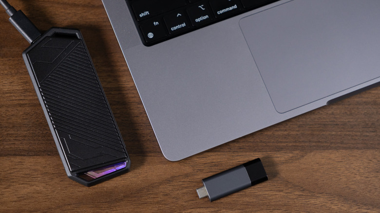 An external hard drive and small flash drive sitting on a desk plugged into a laptop