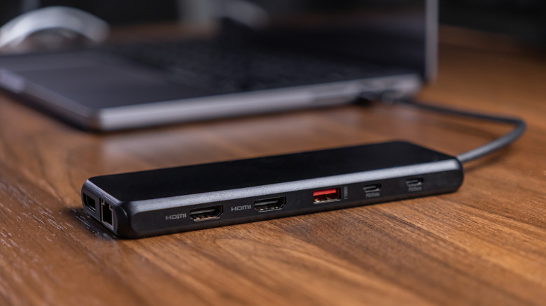 A small docking station sitting next to and plugged into a laptop on a desk