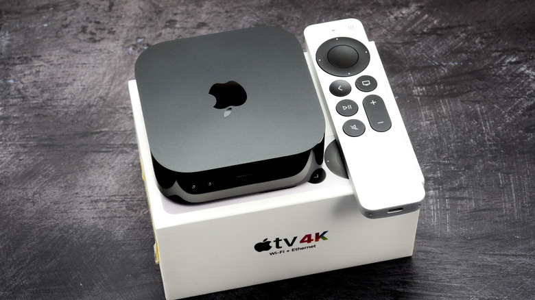 An Apple TV 4K and remote sitting atop its box with what appears to be a brushed-metal background