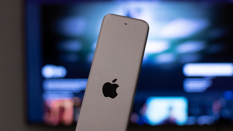 A closeup of a silver Apple TV remote with a television blurred in the background