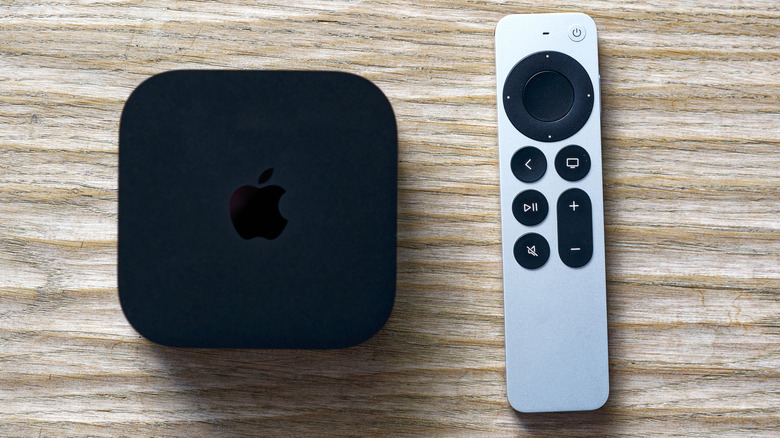 A black Apple TV sitting next to its silver remote, both are sitting on a wooden background