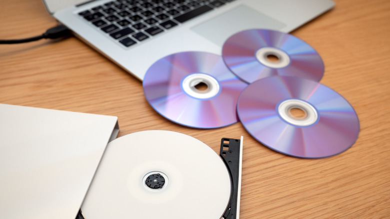 A DVD drive connected to laptop, with one disc in the drive and others scattered nearby