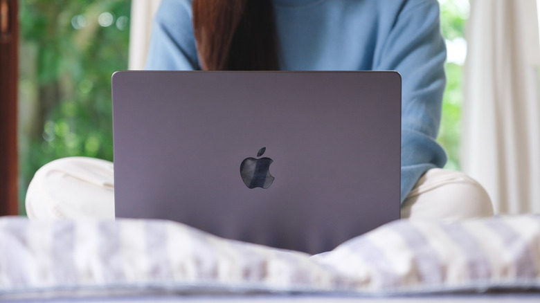 A MacBook sitting atop a striped pillow, a person with long brown hair is behind the machine using it