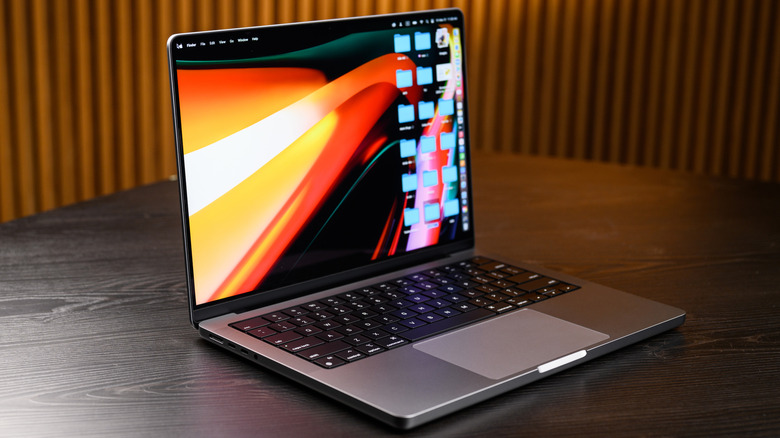 A MacBook sitting on a dark wooden table, the machine is open and displaying its desktop, which contains several folders
