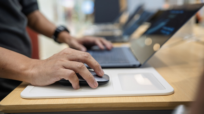 person using a mouse on a white mouse pad, next to a laptop