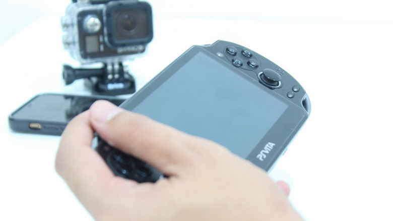 A person holding a PlayStation Vita in one hand on a white background