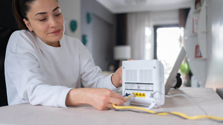 woman plugging ethernet cables into a wi-fi router next to a laptop