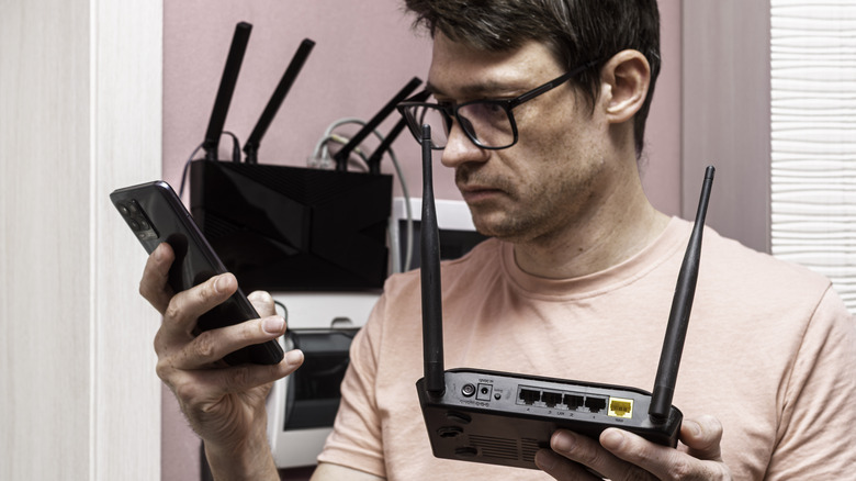 Man changes out an old wireless router while looking at his phone