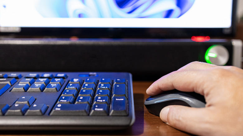 Hand holding a mouse with a keyboard, soundbar, and minitor in view