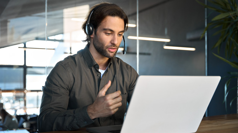 A man in front of a laptop talking into a headset microphone.
