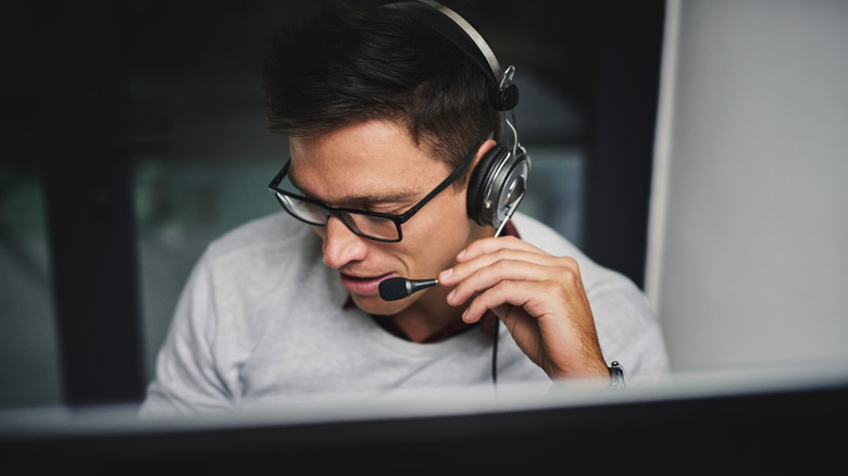 A man in front of a PC using a headset microphone.