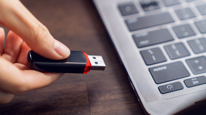 Person holding a USB flash drive next to a laptop