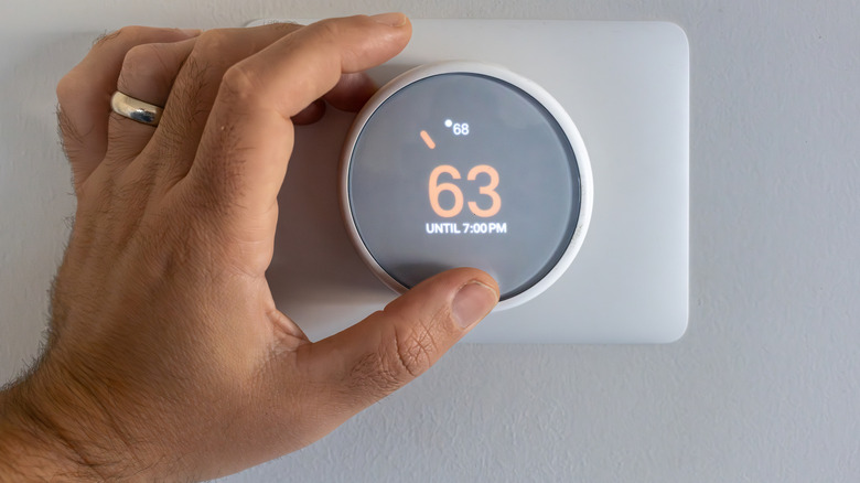 person adjusting a smart thermostat that shows the temperature as 63