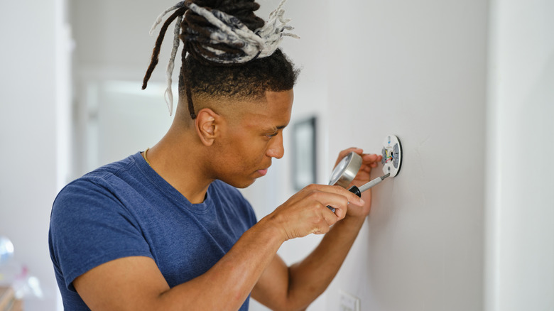 man holding a screw driver installing a smart thermostat at home