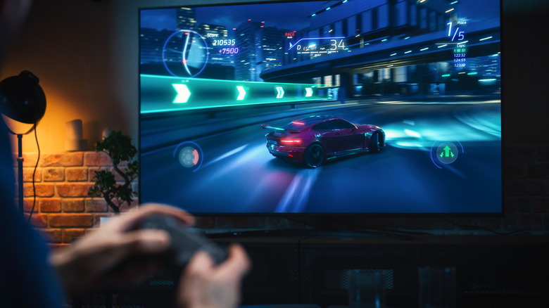 TV with racing game on screen with out of focus hands holding controller in front