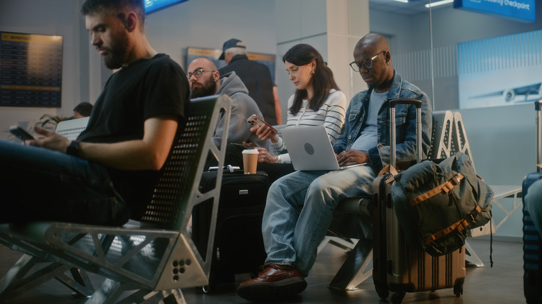 travelers using their smartphones and laptops at the airport
