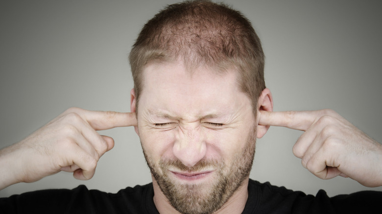 A male person covering their ears with fingers to escape noise