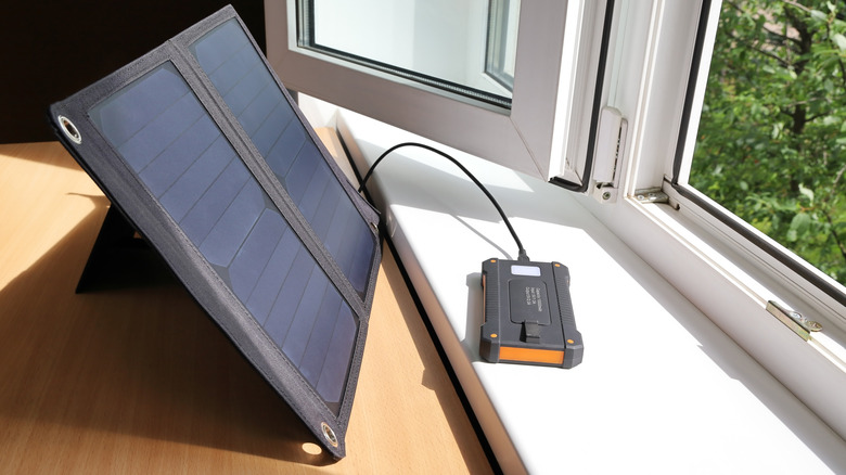 Portable solar panel near an open window and plugged into a mobile device.