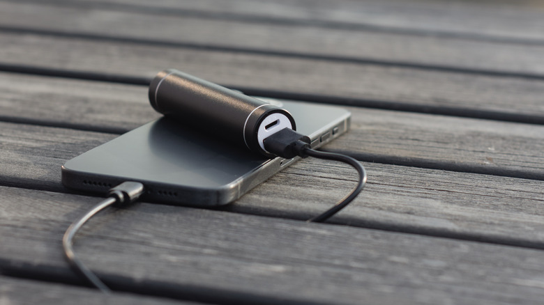 A smartphone being charged using a power bank on a wooden table