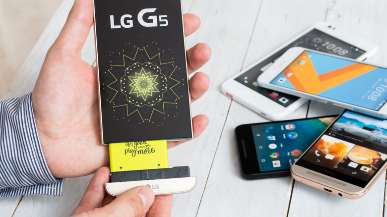 Close-up of a person removing the bottom segment of LG G5 next to other smartphones