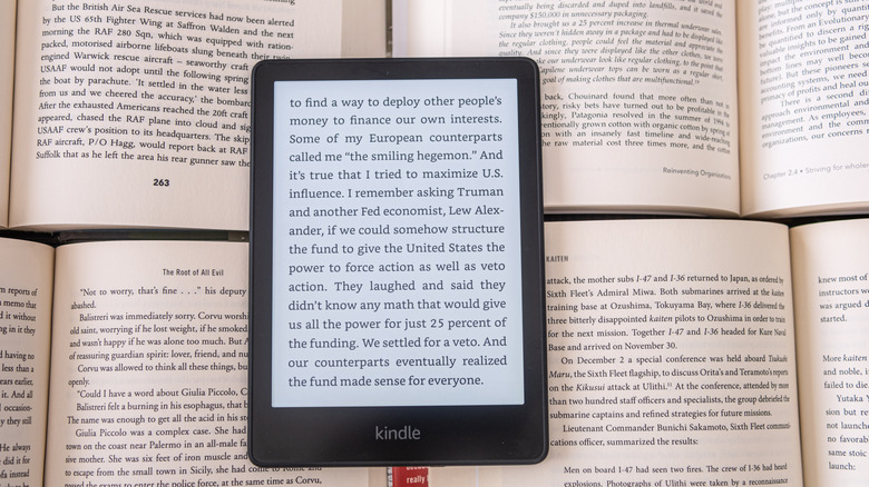 A Kindle displaying the page of a book, the device sits against a background of several open books