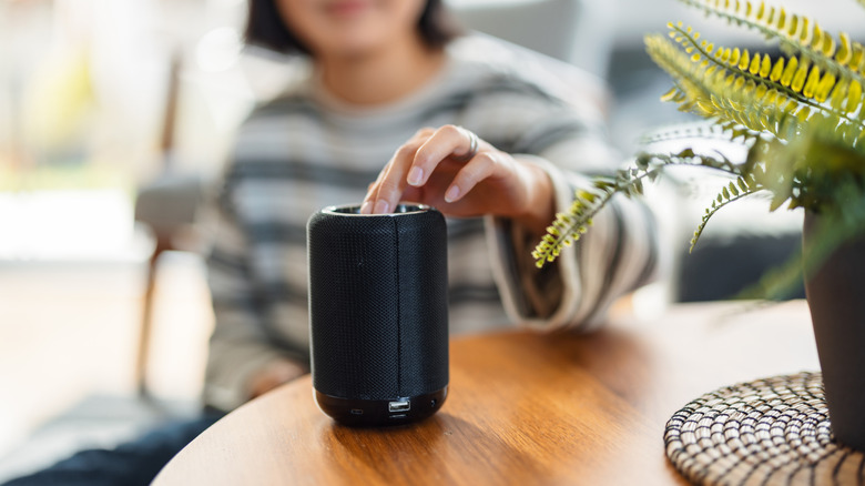 woman uses bluetooth speaker on a table next to a houseplant