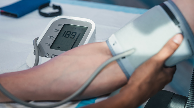 A person with their upper arm strapped, having their blood pressure reading shown on a digital interface