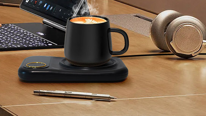 A USB-powered mug warmer sitting on a desk while a woman works
