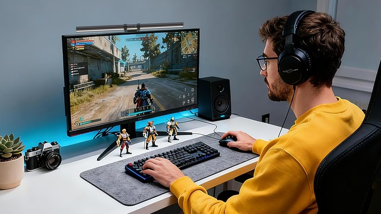 A man playing PC games at a desk with a monitor light bar