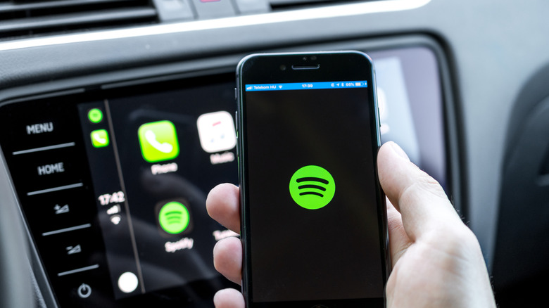 The Spotify logo on an iPhone and on a vehicle display in the background