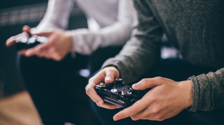 Two people sitting side by side using Xbox controllers.