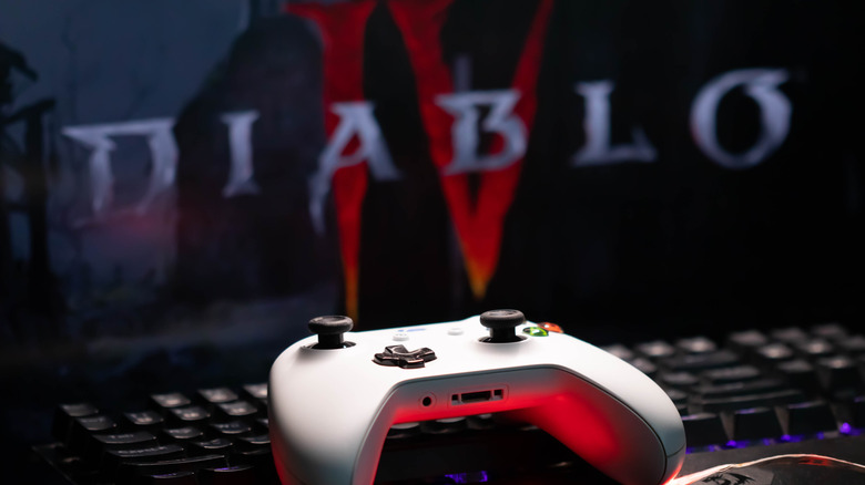 An Xbox controller on top of a keyboard, with "Diablo IV" shown on a screen in the background.