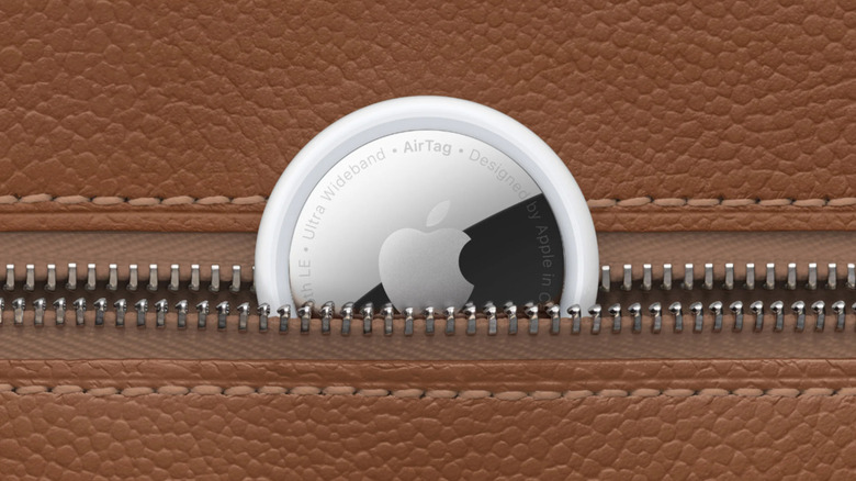 An Apple AirTag peeking out the zipper compartment of a tan bag