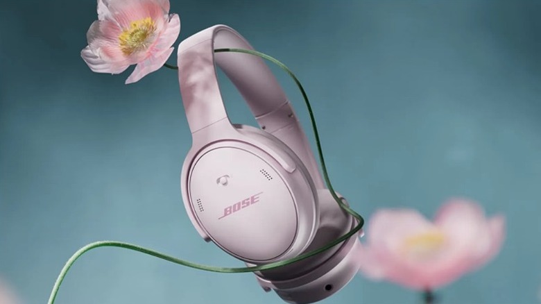 Pink Bose QuietComfort SC headphones entangled with a pink flower against a blue background