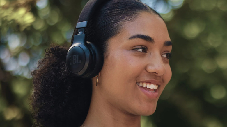 A woman smiling wearing a pair of black JBL Live 675NC headphones