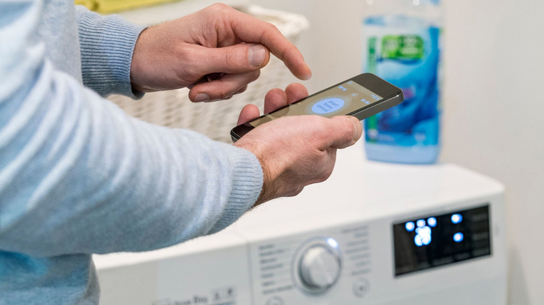 A person using their phone to control a smart washing machine.