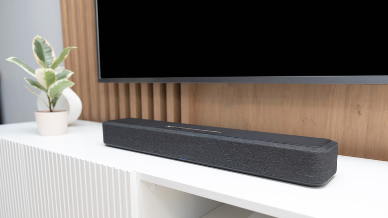 A soundbar placed on an entertainment center. A wall-mounted TV hangs above it.