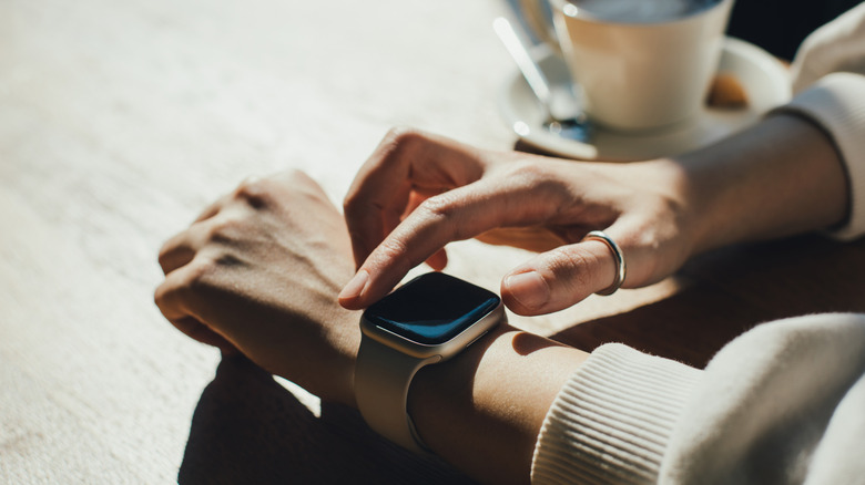 A woman using a smartwatch on a desk, with a mug of coffee beside her hands.