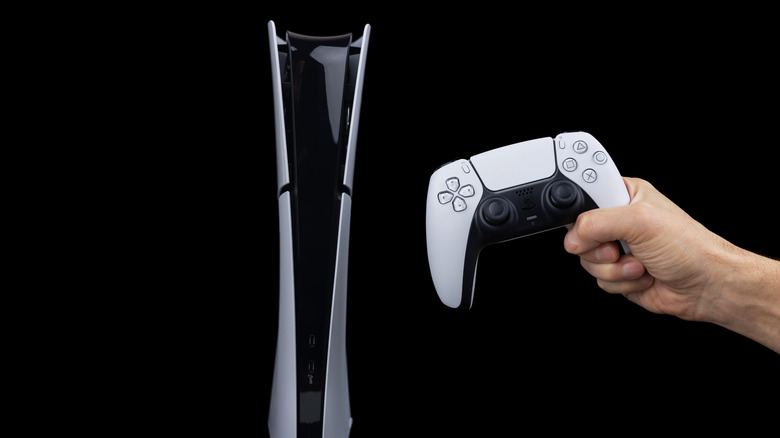 A hand holding a PlayStation 5 controller in front of a PS5 with a dark background