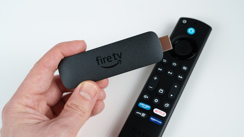 A person holding an Amazon Fire TV Stick above its remote control.
