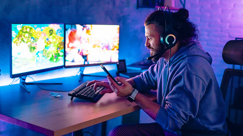 A person playing games on dual-screen setup while using their phone and wearing headphones