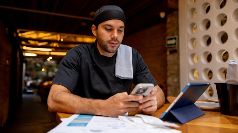 A person using their phone and tablet in tandem while sitting on a wooden desk